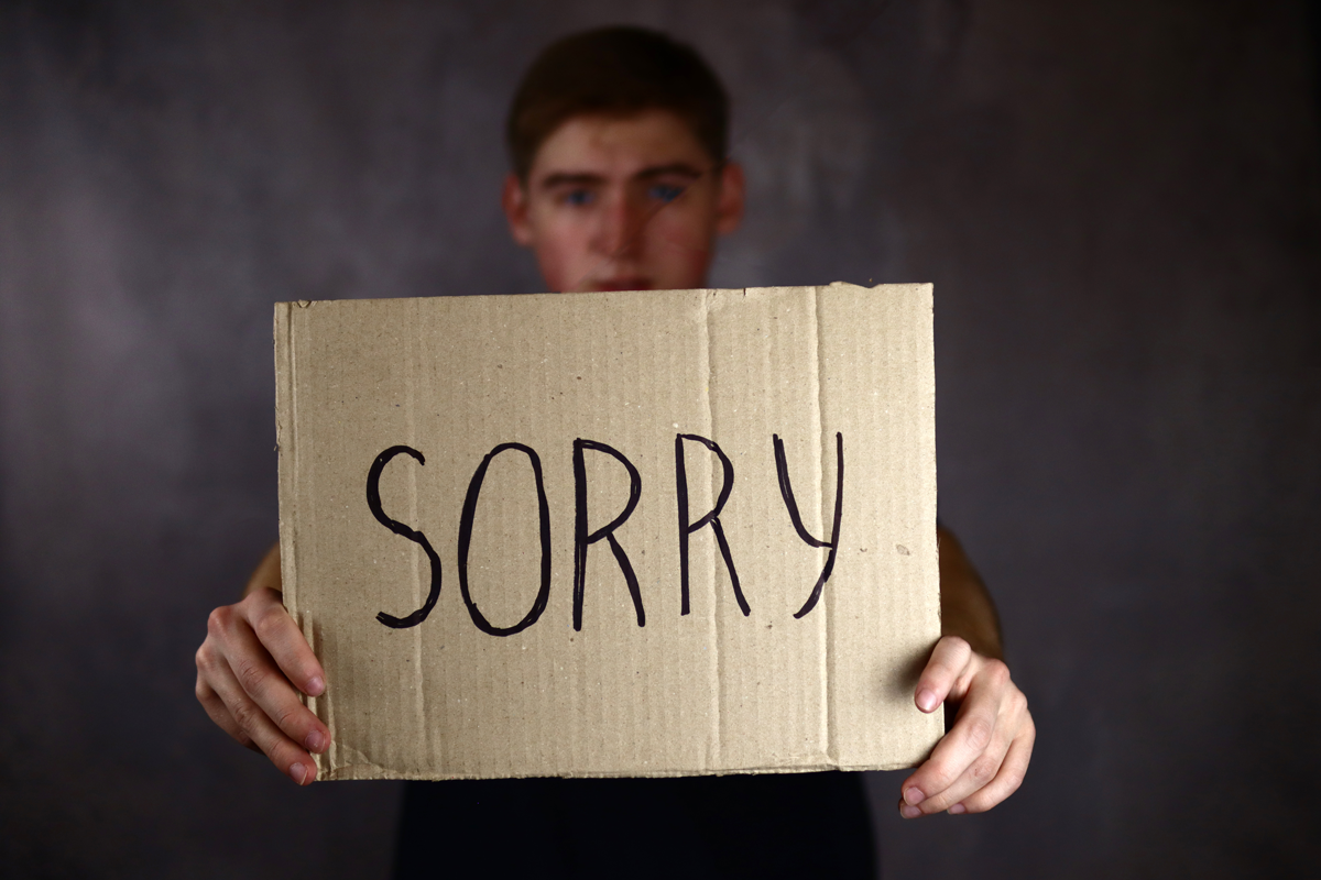teenager holding a sign that says sorry
