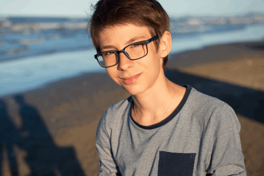 Young boy special needs kid. Cute spectacled smiling happy 12 years old boy at seaside