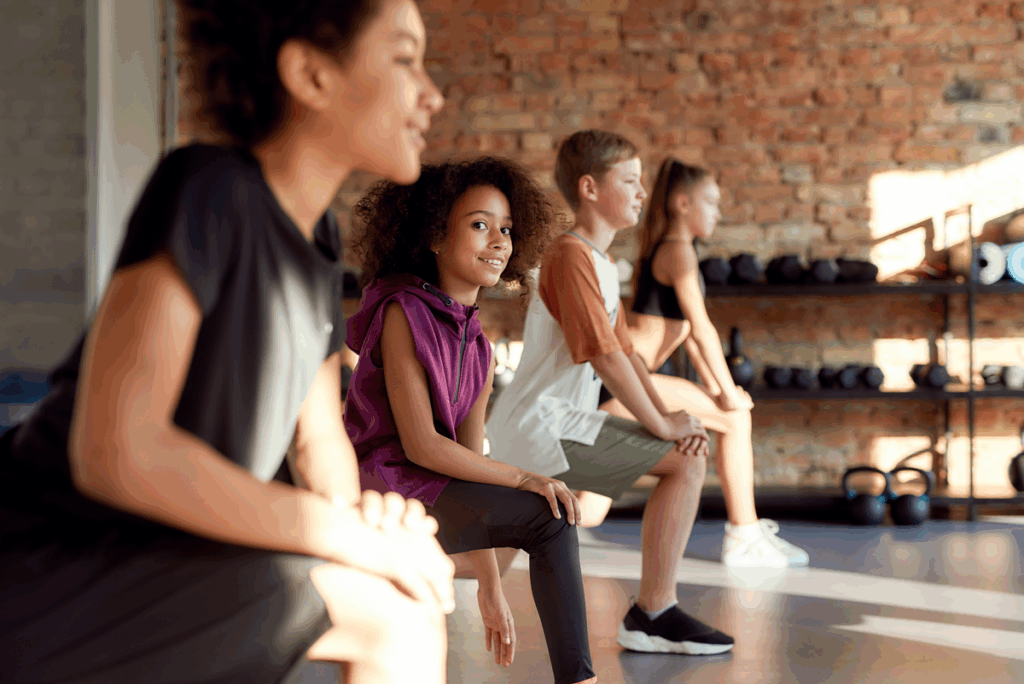 Portrait of a girl smiling at camera while warming up, exercising together with other kids in gym. Sport, healthy lifestyle, physical education ..